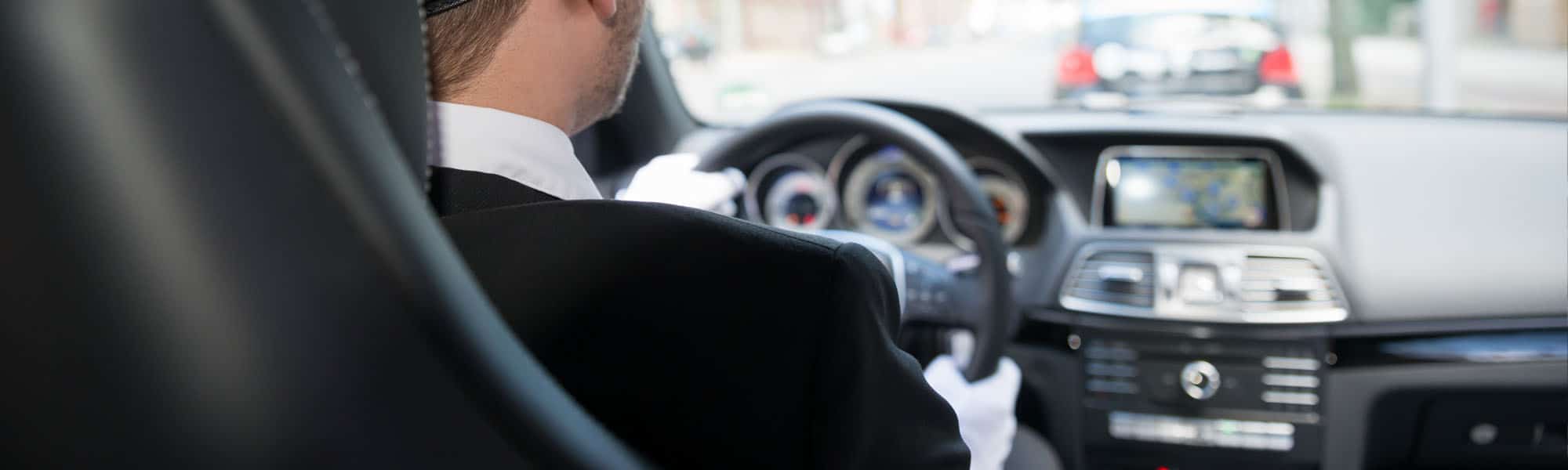 Gloved chauffeur's hands on the steering wheel of an executive car in traffic