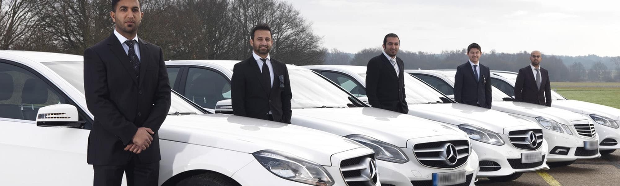 Line-up of uniformed XLNC Cars chauffeurs beside a fleet of white Mercedes executive cars